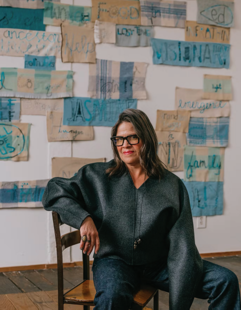 Marie Watt Marie Watt with Untitled—Work in Progress, 2022, consisting of panels from Whitney Sewing Circles. Photographed in Portland, Oregon, December 2022. Styled by Rachael Wang. Watt wears a Toteme sweater from Frances May; Chimala jeans from Frances May; her own glasses and jewelry. Known as Germantown Revival, Cody’s style involves the use of commercially manufactured bright, aniline-dyed wool yarn. She tends to mix traditional Navajo symbols such as the Spider Woman cross (“a symbol of balance,” she says) with personal and pop-culture references like superpixelated video games. “Being a child of the 1980s, I grew up with Atari and the first Nintendo, and all of those influences are definitely evident in the work,” she says, also comparing her line-byline process on the loom to the motion of an inkjet printer. The techno imagery sets her work apart, but that’s far from the only source of innovation. Cody describes the history of Germantown weaving as particularly creative. It originated in 1864, when Navajo peoples from different regions were persecuted by the U.S. military. If they survived the death march known as the Long Walk, they were imprisoned at Fort Sumner, in New Mexico. As supplies, she says, they received brightly colored blankets made from wool milled in Germantown, Pennsylvania. Navajo weavers then unraveled these blankets and rewove them into their own styles, creating the mash-ups called samplers as patterns were “exchanged among the weavers from different regions who were corralled together,” she says. “That’s what I’m really drawn to—the idea that during such a dire time, the creative spirit of people couldn’t be broken and couldn’t be stolen.” 